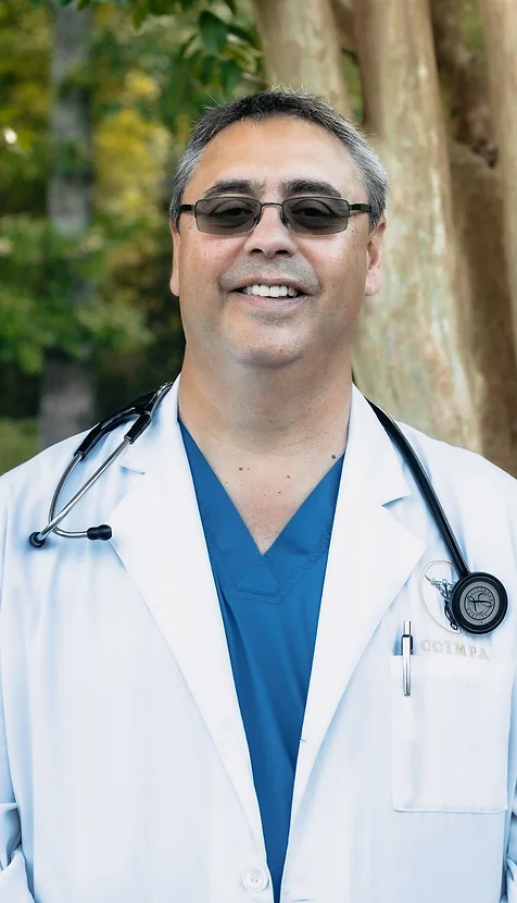 DR. JOSE IGNACIO ROS M.D. of Coastal Carolina Aesthetics poses smiling wearing his doctor's coat and stethoscope.