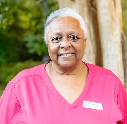 Veronica, a member of the front desk staff at Coastal Carolina Aesthetics, poses outside smiling wearing pink scrubs.